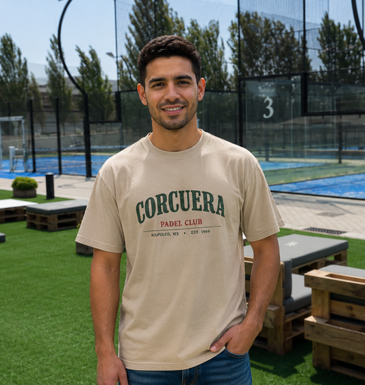 Man wearing a beige t-shirt with 'Corcuera Padel Club' text, standing in an outdoor setting.