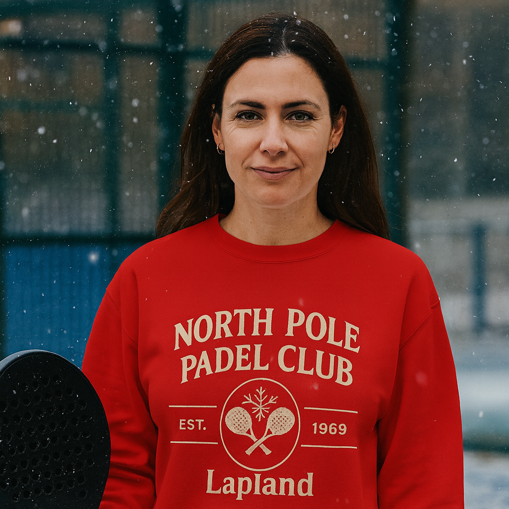 Woman wearing a red 'North Pole Padel Club' sweatshirt holding a paddle on a snowy day.